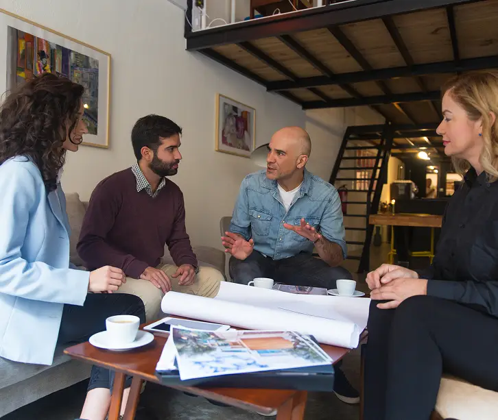 Man presents blueprints; clients listen; modern office.