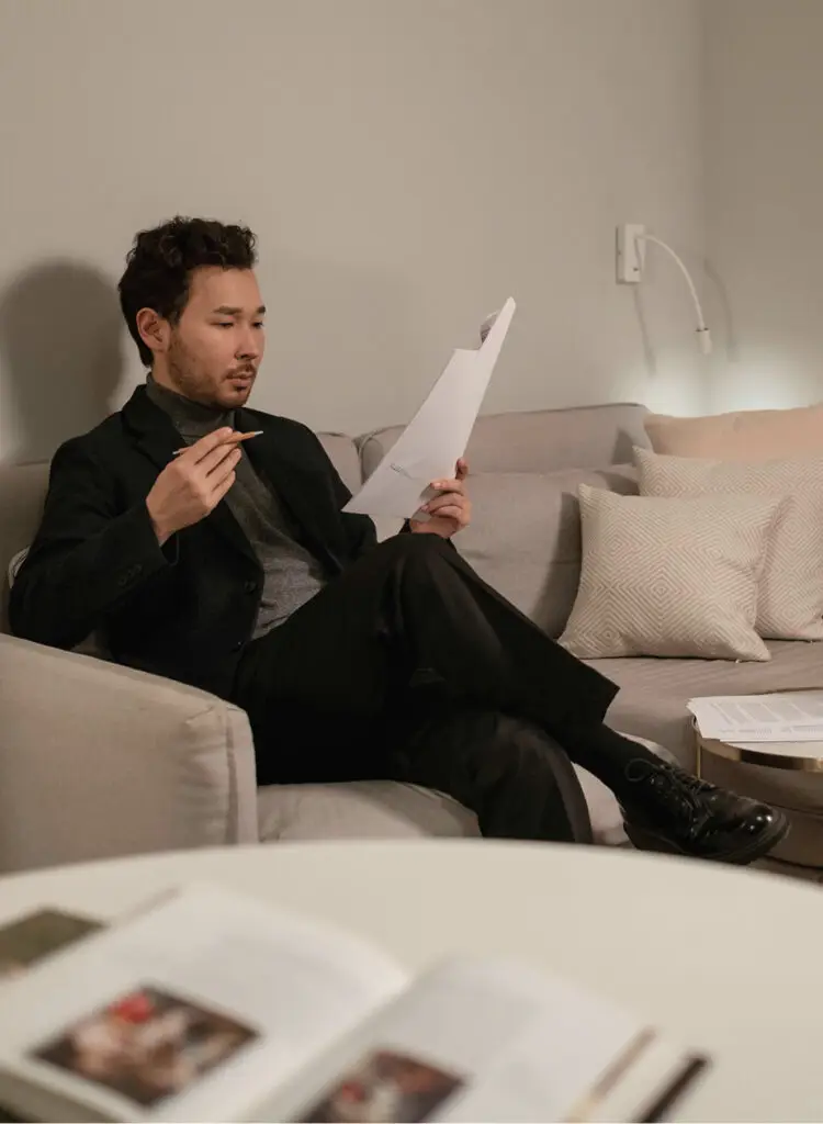 Man reviews documents, pen in hand, while sitting on a couch.